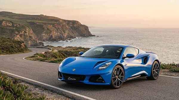 Blue Lotus Emira sports car parked on a scenic winding coastal road next to the ocean.
